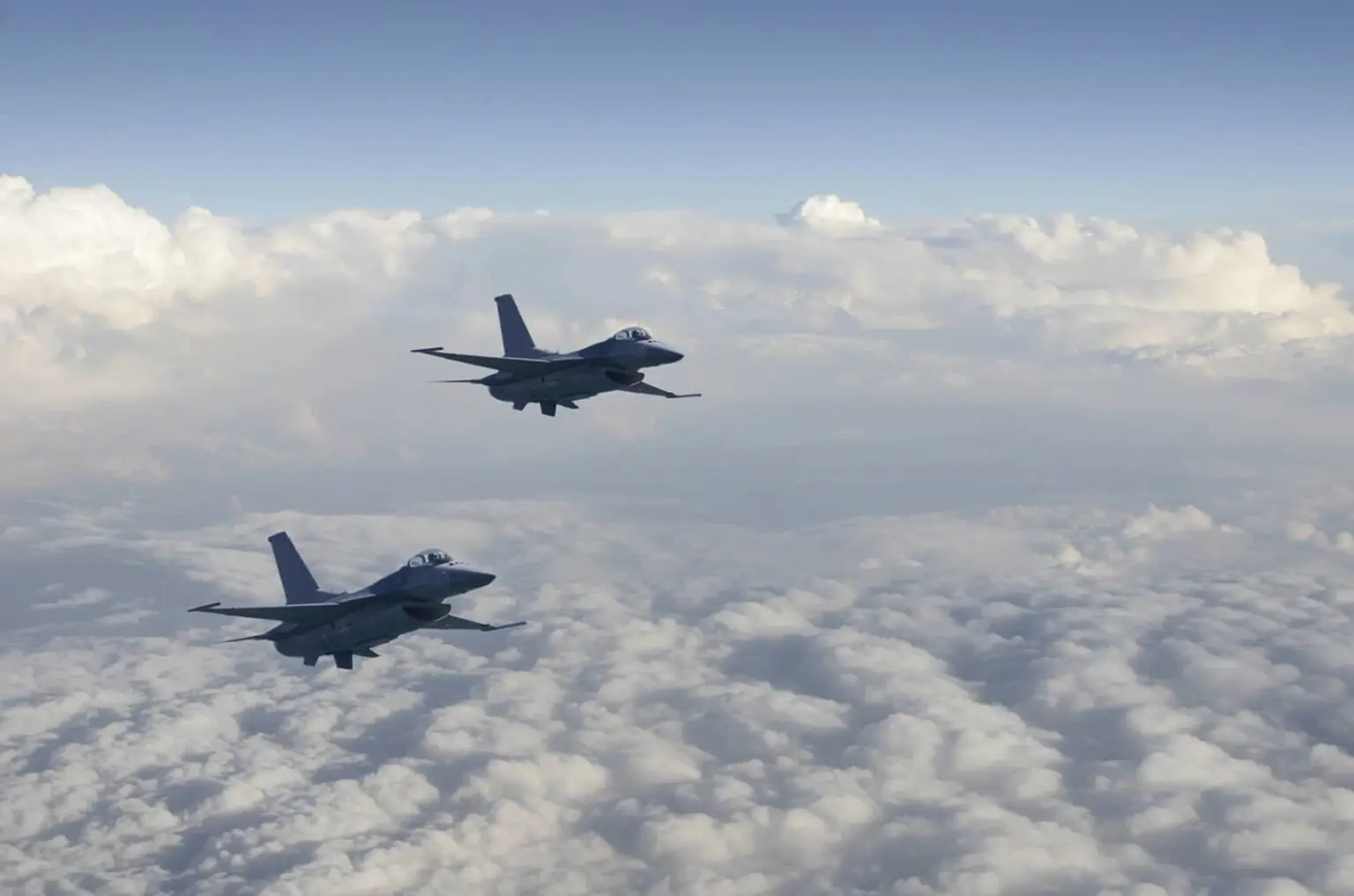 An image showing 2 air force planes flying in formation above the clouds on a sunny day.